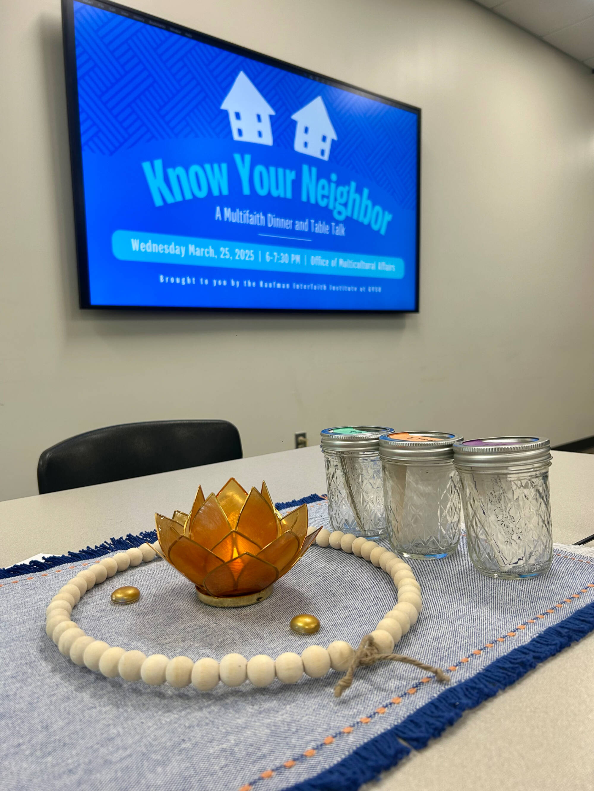 A decorative centerpiece with three jars of conversation cards and the Know Your Neighbor logo on the screen in the background.